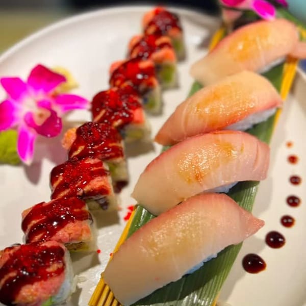 Kameya Sushi platter with nigiri and sushi rolls drizzled with red sauce, garnished with orchids.
