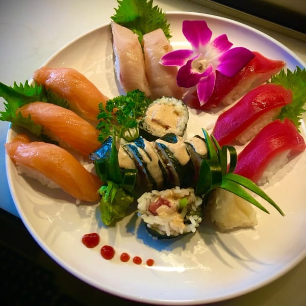 A white plate of Kameya Sushi's nigiri and sushi rolls, garnished with a purple orchid.