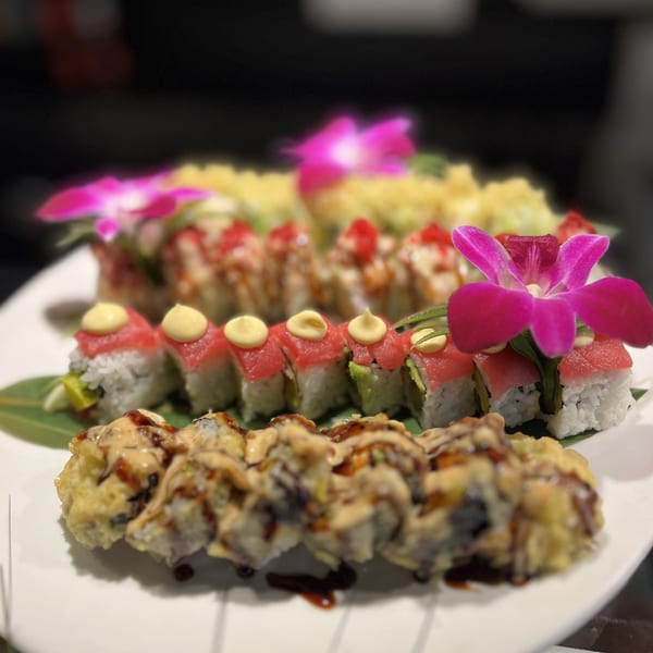 A platter of Kameya Sushi rolls, including tuna, avocado, and tempura, garnished with orchids.