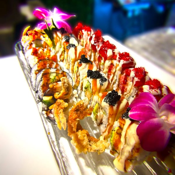 A long platter of Kameya Sushi rolls, garnished with bright pink orchids, black and red roe.