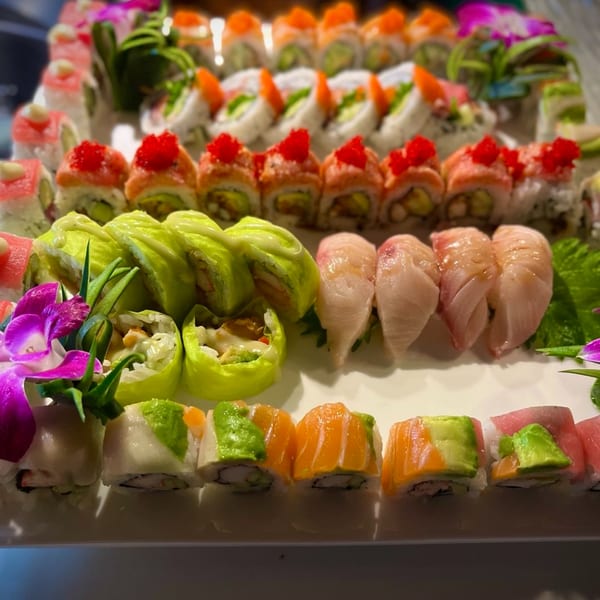 A vibrant platter of Kameya Sushi rolls, including salmon, tuna, and avocado, garnished with orchids.