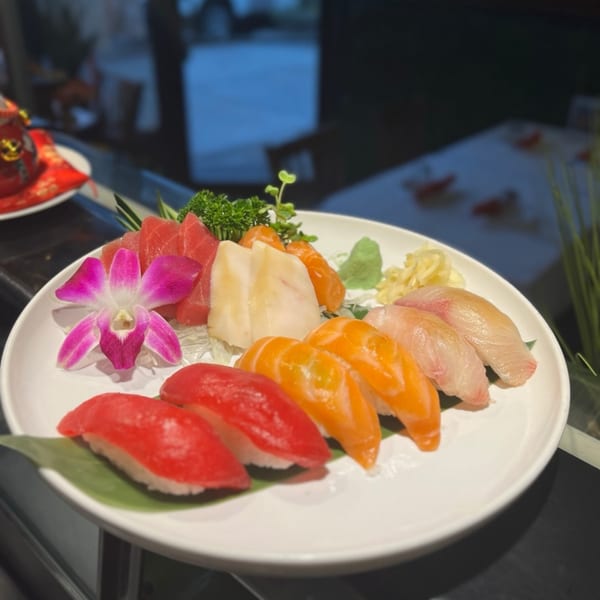 A white plate of Kameya Sushi's colorful nigiri and sashimi, garnished with a pink orchid.
