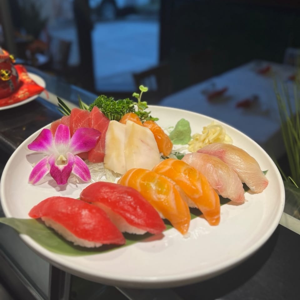 A white plate of Kameya Sushi's colorful nigiri and sashimi, garnished with a pink orchid.